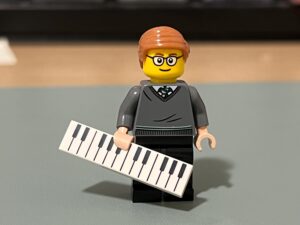 Lego figurine wearing glasses and holding a piano, resembling Mr. Hoffman